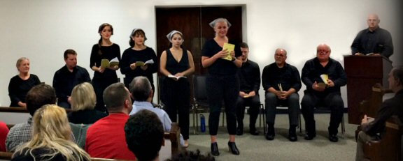ten people dressed in black are in fron of an audience. four of them are standing.